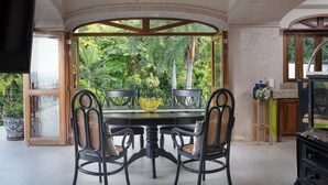 A dining area with a table and chairs, a ceiling fan, and a view of greenery outside.
