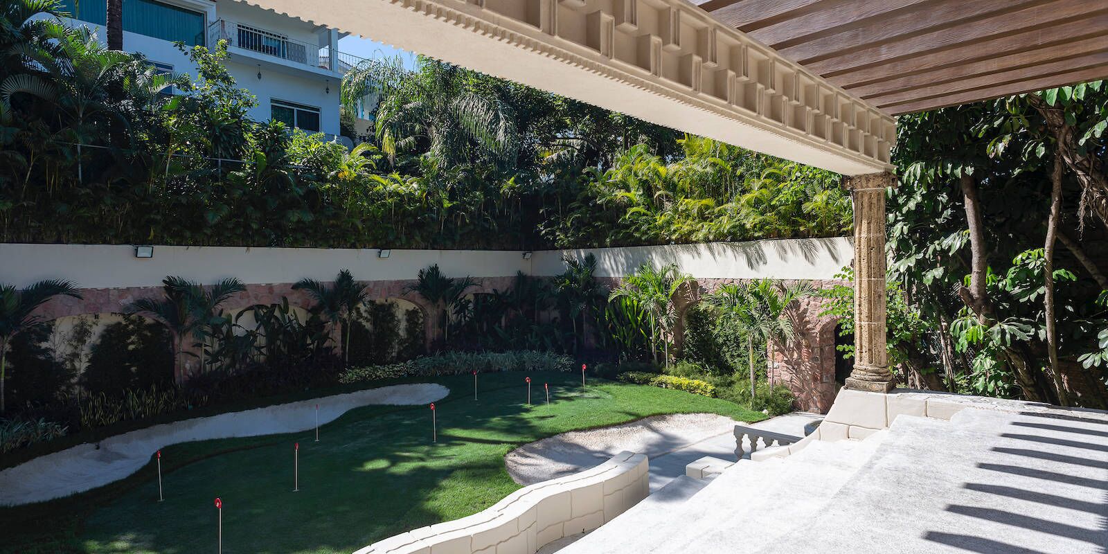 A covered outdoor area with a green lawn, a stone wall, and a pergola.