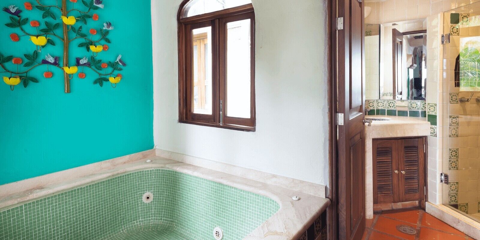 A bathroom with a green-tiled bathtub, a wooden door, and a window.