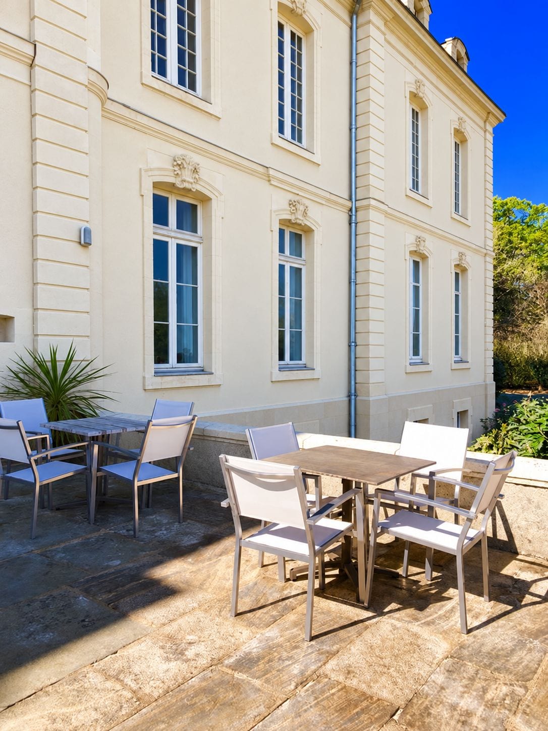Une terrasse extérieure avec une table et des chaises, un bâtiment doté de grandes fenêtres et un ciel bleu dégagé.