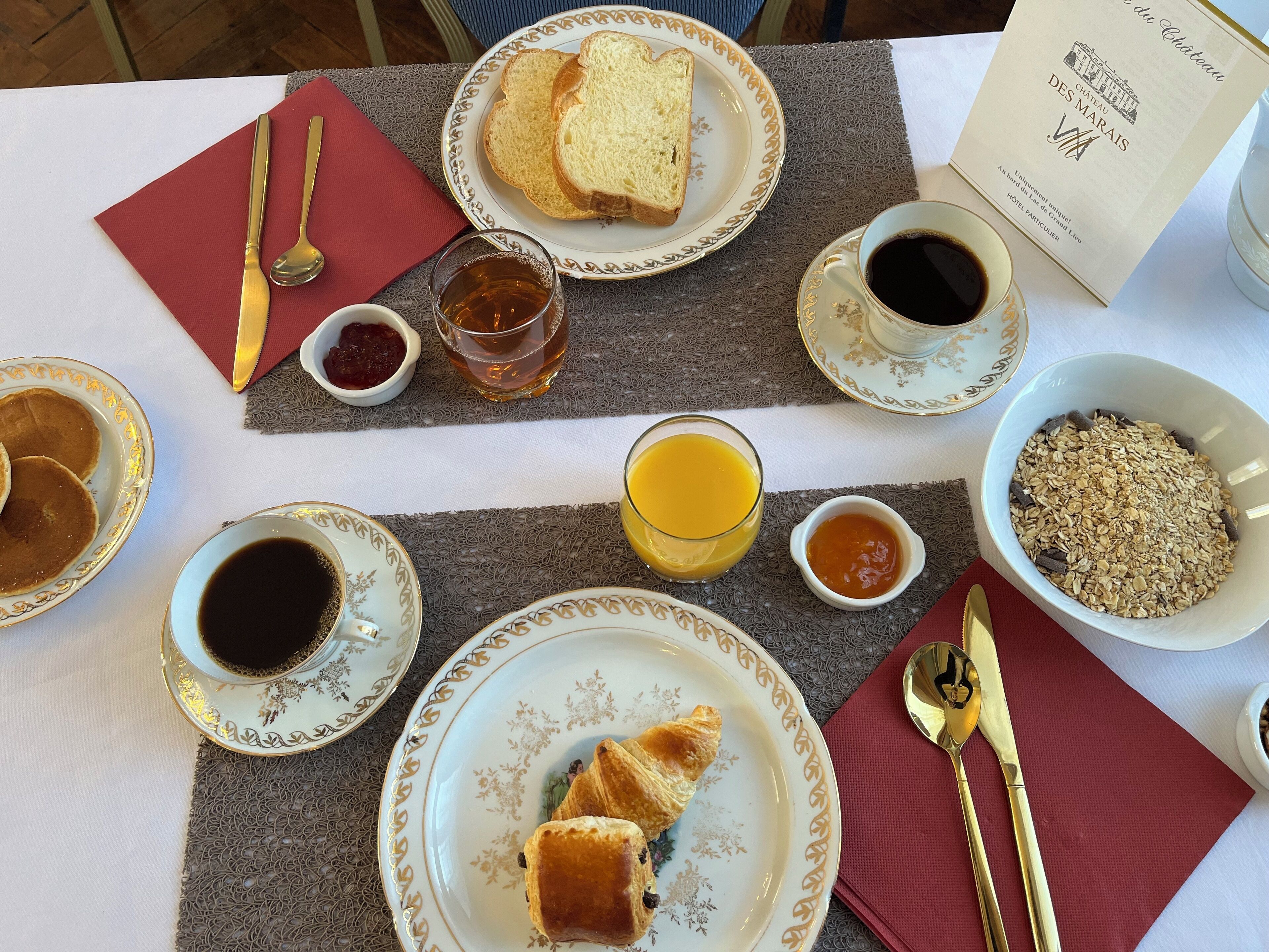 A breakfast setting with bread, croissants, coffee, tea, and cereal.