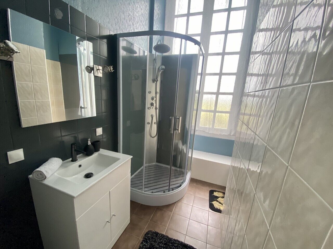 Un baño moderno con ducha envuelta en vidrio, tocador blanco y un espejo grande.