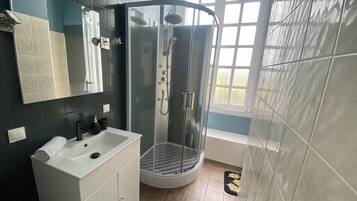 Un baño moderno con ducha envuelta en vidrio, tocador blanco y un espejo grande.