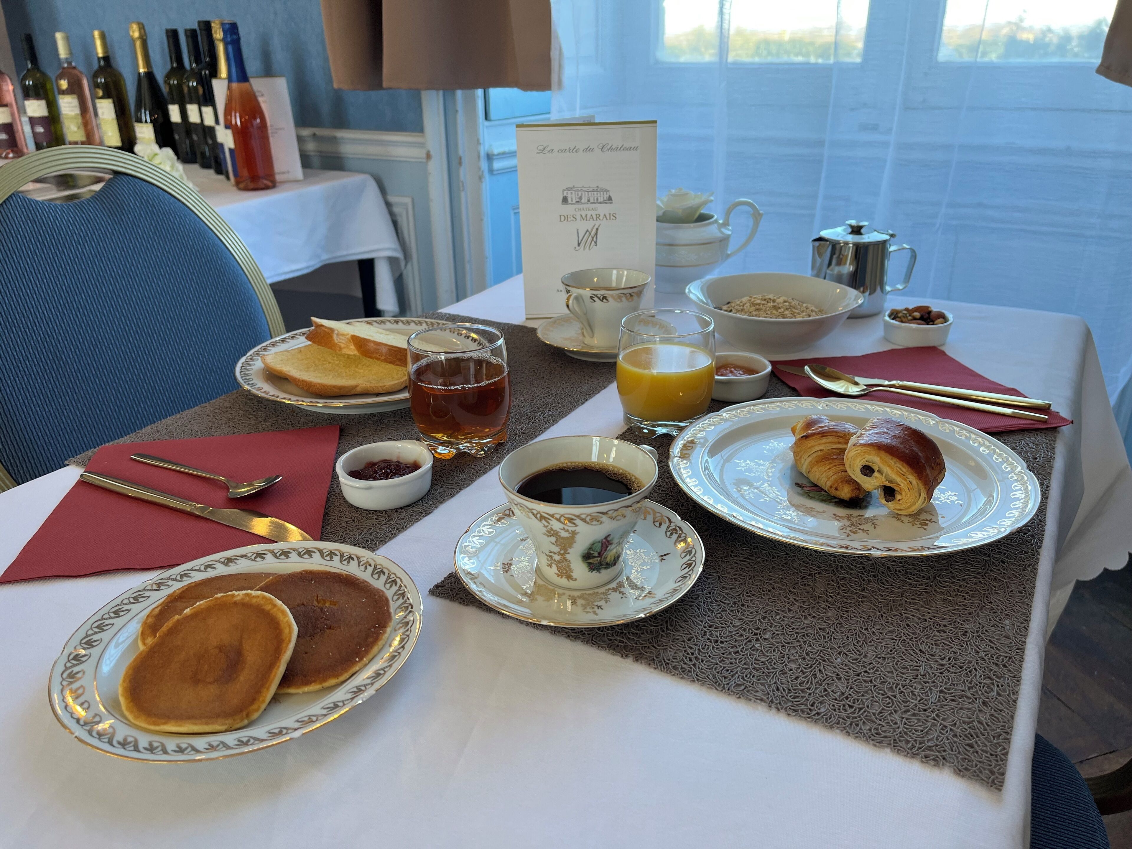 A breakfast table with pancakes, croissants, coffee, and juice.
