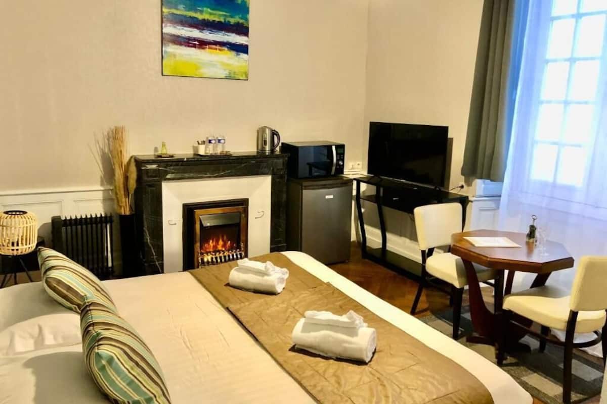 Une chambre d’hôtel équipée d’un lit, d’une cheminée, d’un bureau, d’une télévision et d’une fenêtre.