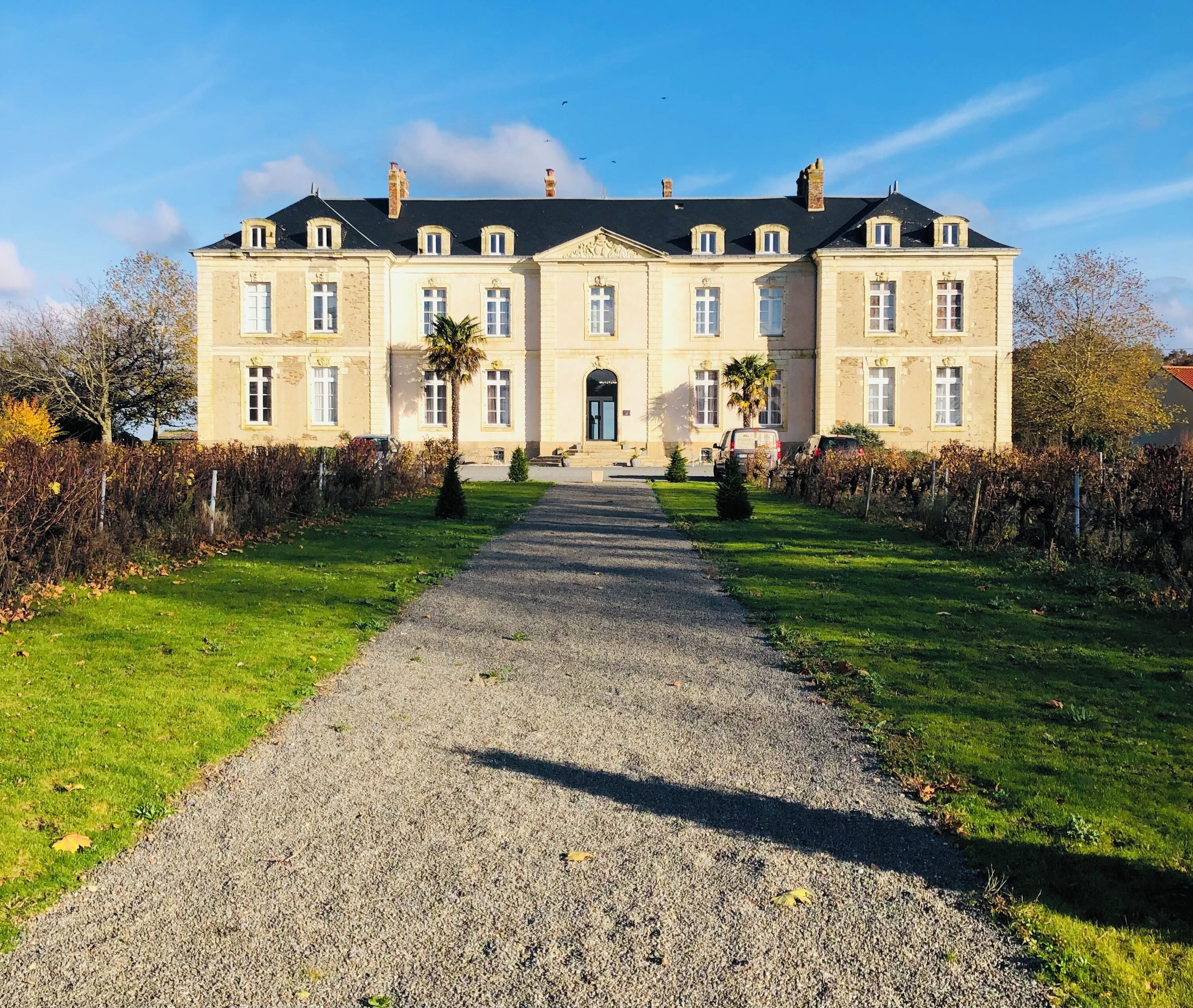 A large, historic building with a symmetrical facade, a central entrance, and a gravel pathway leading to it.