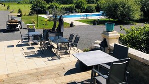 Une terrasse avec des sièges extérieurs, une piscine et une vue sur un paysage verdoyant.