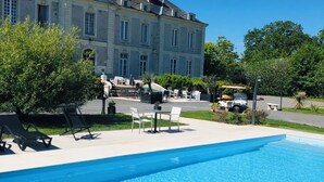Une piscine avec des chaises longues, une table et un bâtiment en arrière-plan.