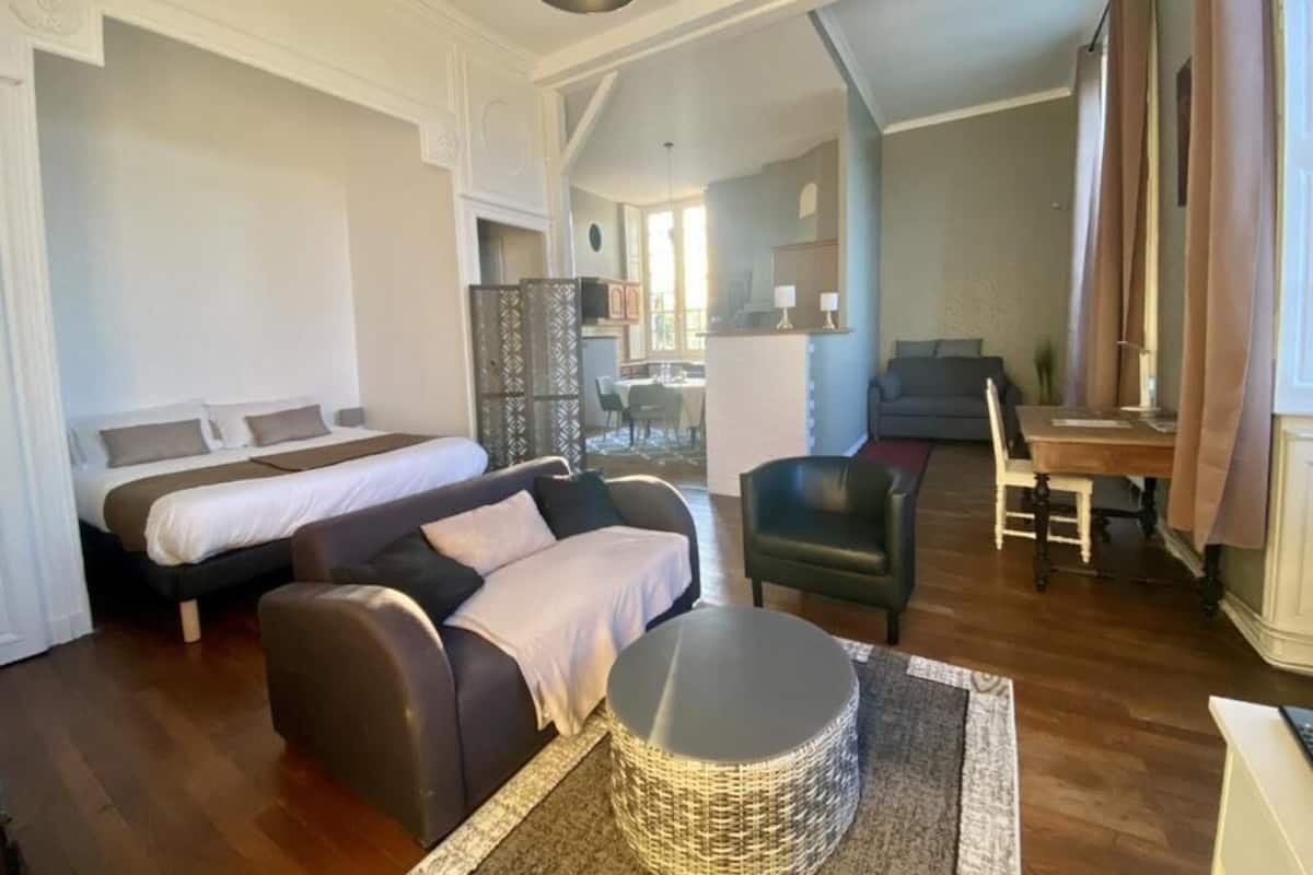 Une chambre d’hôtel moderne avec un grand lit, un canapé, une table à manger et un coin cuisine à l’arrière-plan.