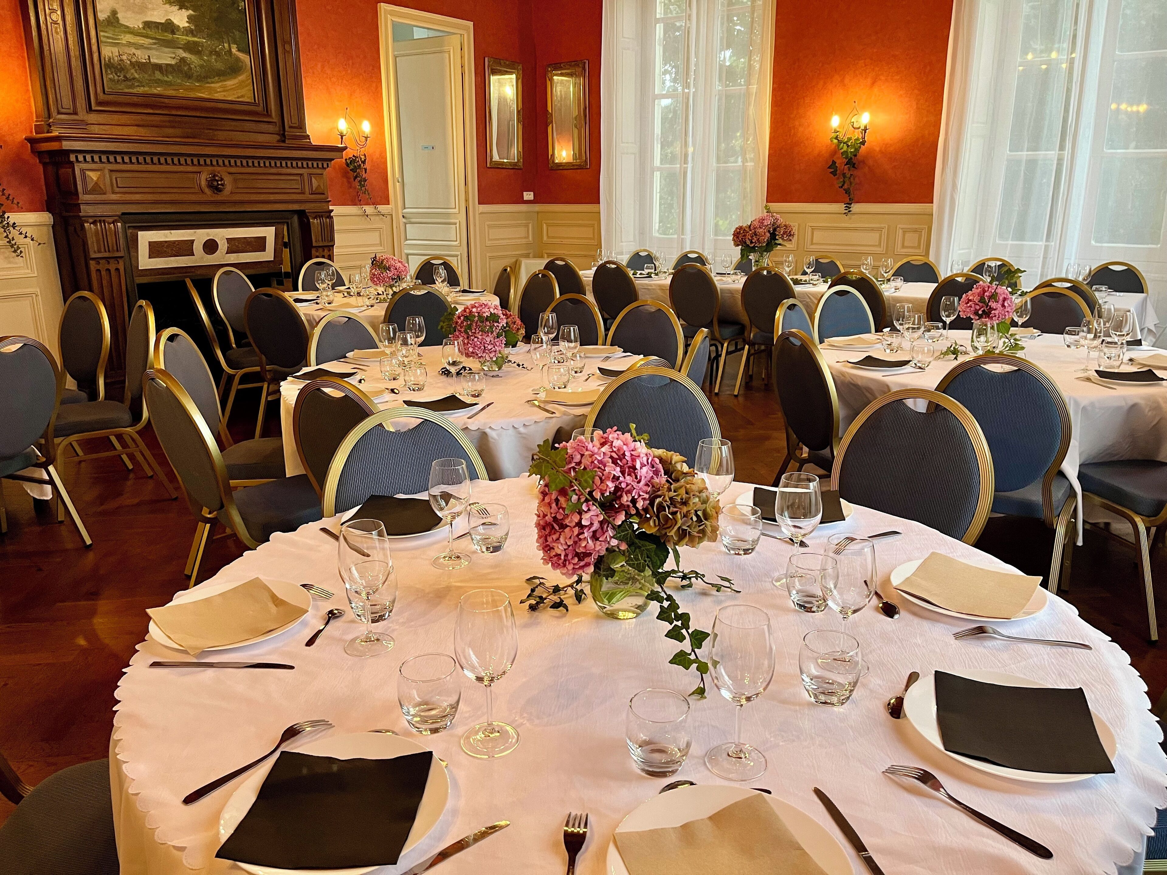 A formal dining room with multiple tables set for a meal, each with chairs, plates, cutlery, and glasses.