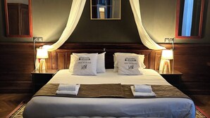 Une chambre d’hôtel avec un grand lit, deux tables de chevet, un lit à baldaquin, un miroir et un tapis à motifs.