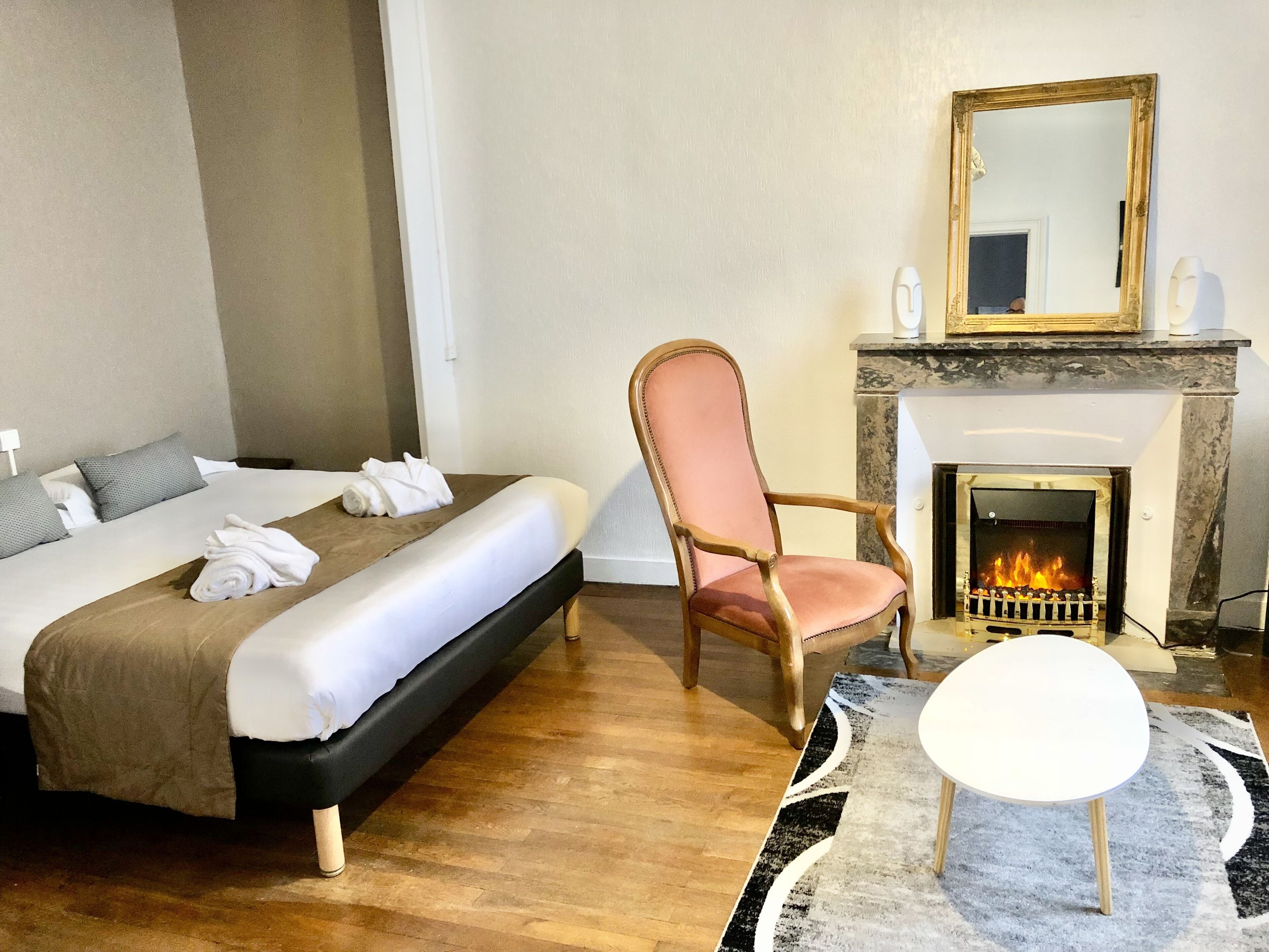 A hotel room with a bed, a chair, a fireplace, and a small table.