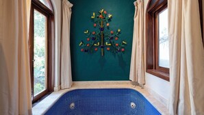 Habitación con una bañera de azulejos azules, una pared verde mar y una escultura de árbol decorativa.