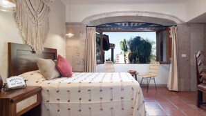A bedroom with a bed, a nightstand, a chair, a wooden table, and a TV.