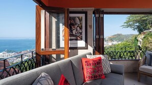 A balcony with a sofa, a red pillow, and a framed picture. - Rent the Entire Floor at Luxury Resort: 5th Floor Suites Spectacular Ocean Views (Puerto Vallarta)