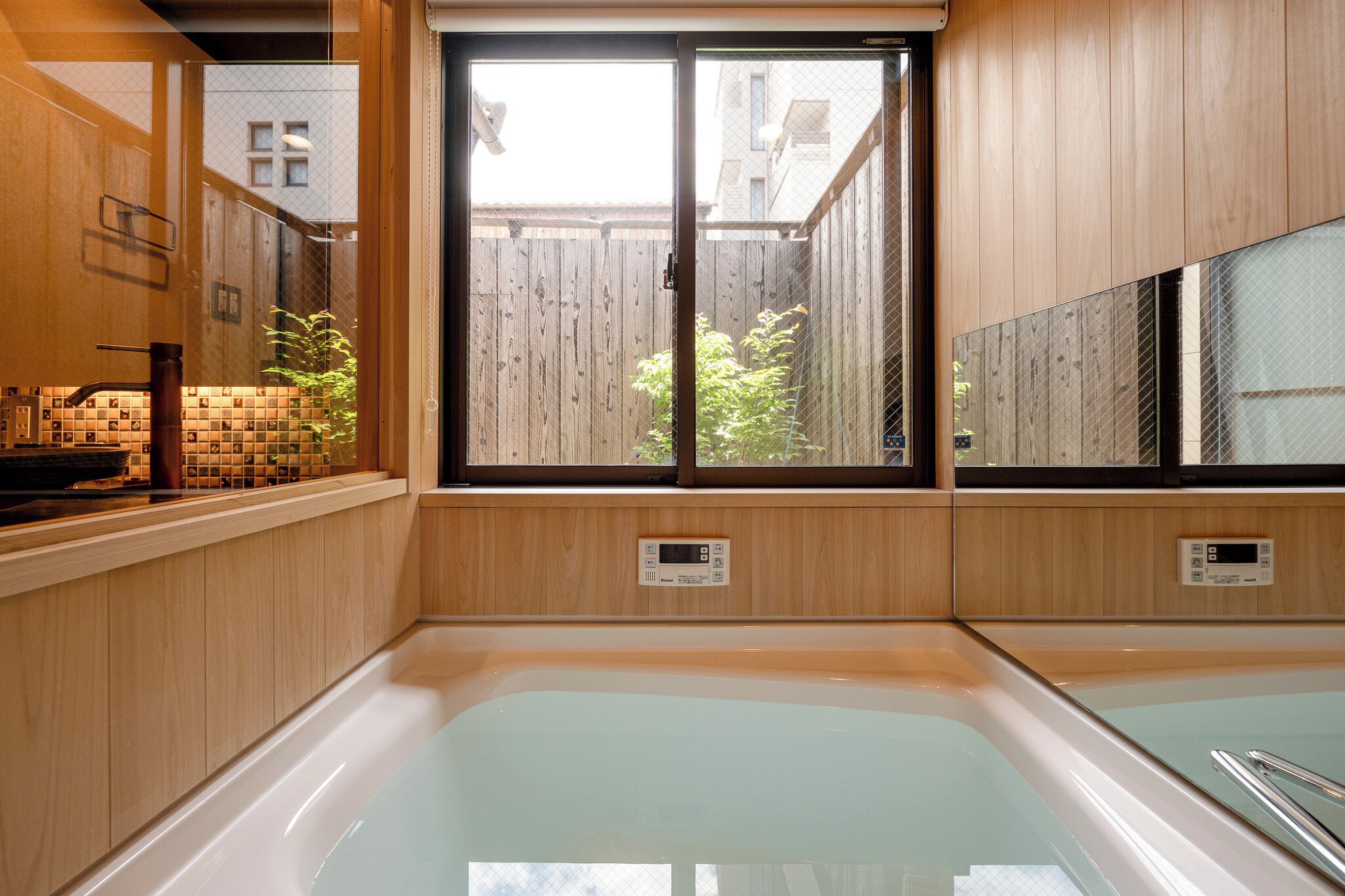 Un baño moderno con una bañera grande, paneles de madera y vistas a un patio trasero a través de un ventanal.