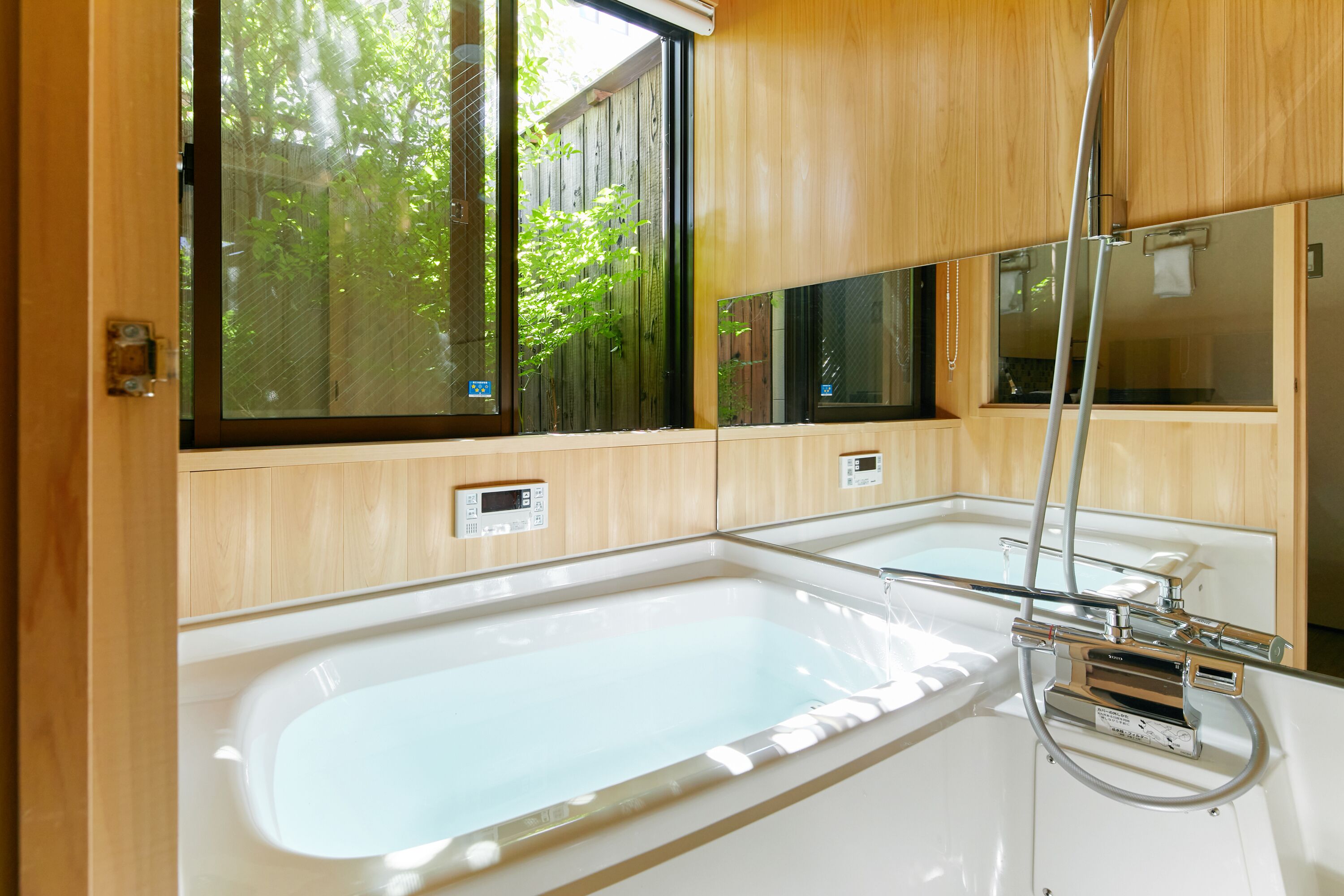 A modern bathroom with a large bathtub, wooden cabinetry, and a window providing a view of greenery.