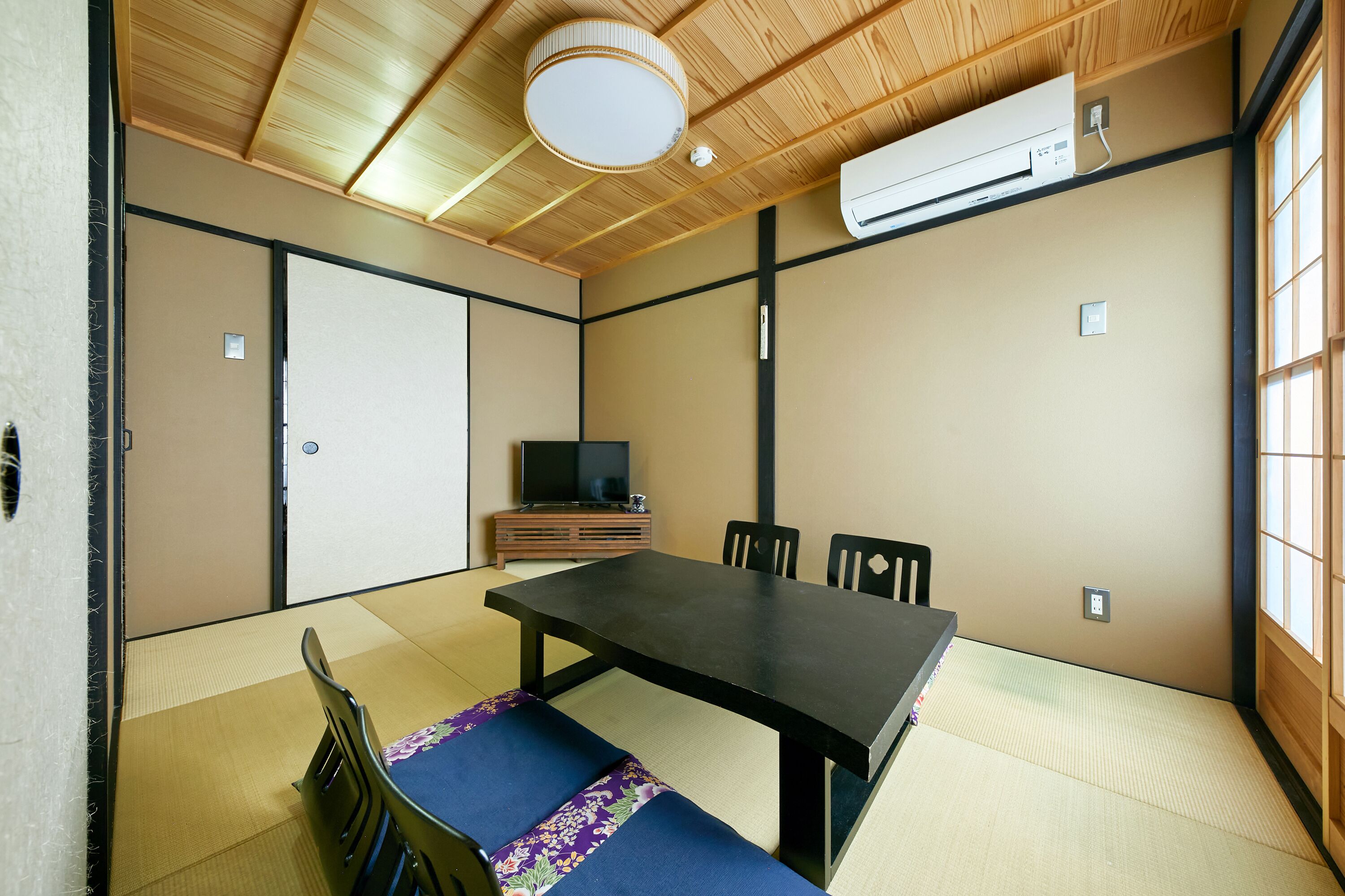 A traditional Japanese room with tatami flooring, a low table, and black chairs.