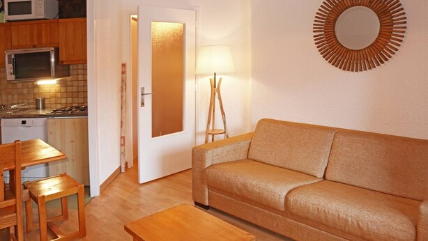 A compact living space with a sofa, a wooden coffee table, a dining table with chairs, a microwave, a stove, and a decorative mirror.