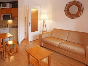 Un espace de vie compact comprenant un canapé, une table basse en bois, une table à manger avec des chaises, un four à micro-ondes, une cuisinière et un miroir décoratif.