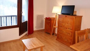 A room with a wooden table, a wooden cabinet, a television on a wooden stand, and a window with a red curtain.