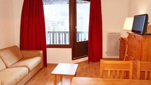 A cozy room with a sofa, a wooden table, a TV on a cabinet, and a window with curtains.