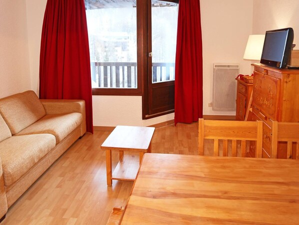 Une pièce chaleureuse avec un canapé, une table en bois, un téléviseur posé sur un meuble et une fenêtre avec des rideaux.
