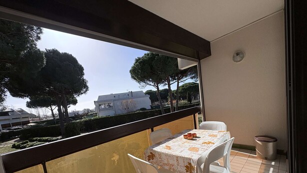 A balcony with a table and chairs, a view of trees and buildings, and a tiled floor. - Cozy Studio Cabin with Terrace & Parking, 4 Sleeps, Near Beach, Le Grau-du-Roi (Le Grau-du-Roi)