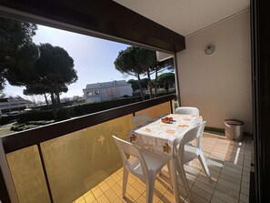 Un balcon avec une table et des chaises, une vue sur les arbres et les bâtiments, et un sol carrelé.