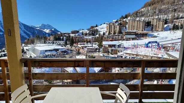 A view from a balcony with a table and chairs, overlooking a snowy mountain town with buildings and a ski slope.