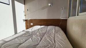 A neatly made bed with a wooden headboard, a wall-mounted light, and a window with blinds.