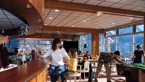 A bar area with wooden bar counter and stools, large windows with mountain views, and a pool table in the background.
