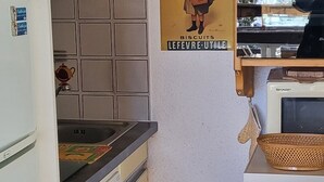 A compact kitchen with a refrigerator, a stove, a sink, and a microwave. There is a poster on the wall advertising biscuits.