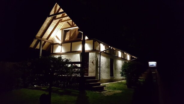 Ein Gebäude mit einem steilen Satteldach, einer sichtbaren Treppe, die zum Eingang führt, und einem kleinen Fernseher, der an der Außenwand befestigt ist.