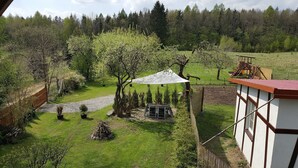 Ein Garten mit einer Holzterrasse, einem weißen Sonnenschirm und einem eingezäunten Bereich mit einem Feldweg.