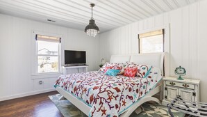 A bedroom with a bed, a TV, a clock, and a window.