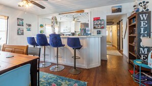 A kitchen with white cabinets, a bar area with blue bar stools, a ceiling fan, and a 'WELCOME' sign.