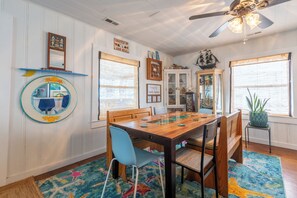 A dining area with a wooden table, blue chairs, a colorful rug, and a ceiling fan.