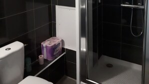 Une salle de bain avec une douche à parois de verre, des toilettes et une petite étagère contenant des articles de toilette.