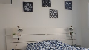 Une chambre à coucher avec une tête de lit blanche, une couvre-lit bleue et blanche à motifs et trois assiettes décoratives accrochées au mur.