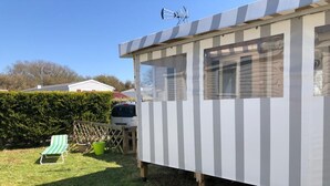 A mobile home with a striped exterior, a small deck, and a green lawn chair. - Mobil Home 3 chambres (Port-Bail-sur-Mer)