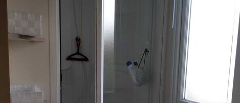 Et badeværelse med et brusebadekar i glas, toilet og et vindue med naturligt lys.