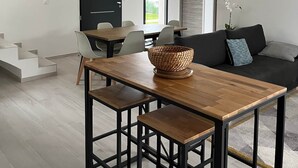 Ein modernes Wohnzimmer mit einem Holzesstisch, schwarzen Metallstühlen, einem gewebten Korb und einer schwarzen Couch mit Kissen.