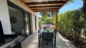 Eine Außenpatio mit Esstisch und Stühlen, einem Grill und einer Pergola darüber.