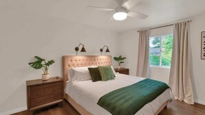 A bedroom with a tufted headboard, two bedside tables with lamps, a large window with curtains, and a green throw blanket.