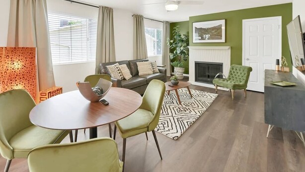 A living room with a sofa, a dining table with chairs, a fireplace, and a green accent wall.