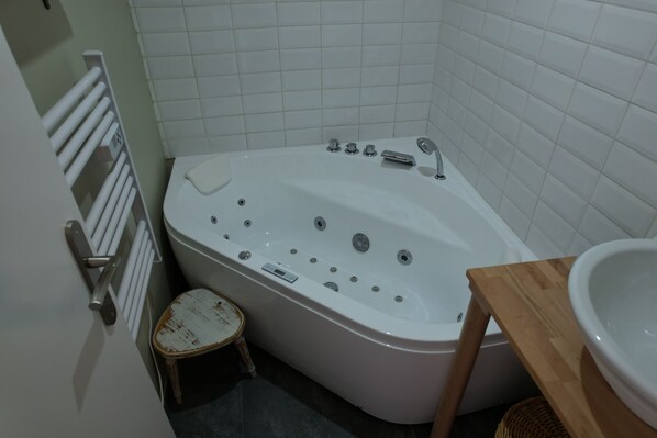 A bathroom with a bathtub, a wooden stool, a sink, and a towel rack.