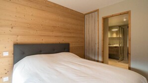 Un dormitorio con una pared de madera, una cama y un baño visible a través de una puerta abierta.