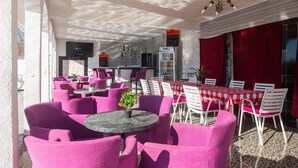 An outdoor seating area with round tables and chairs, a bar area with a counter and shelves, and a red curtain backdrop.