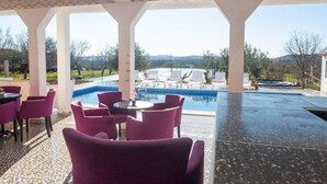 A covered outdoor area with a pool, seating, and a view of the landscape.